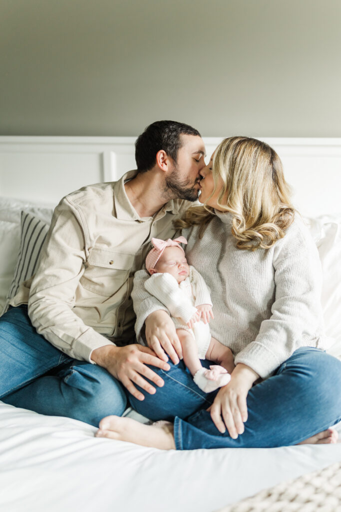 A mom and dad share a kiss while sitting on their bed with their baby girl.
Central Illinois Newborn Photographer.
Amanda Banik Photography